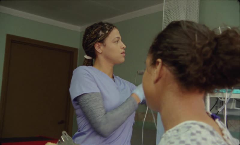 Nurse enters a room where a young woman wearing a hospital gown is sitting on a bed filling a form