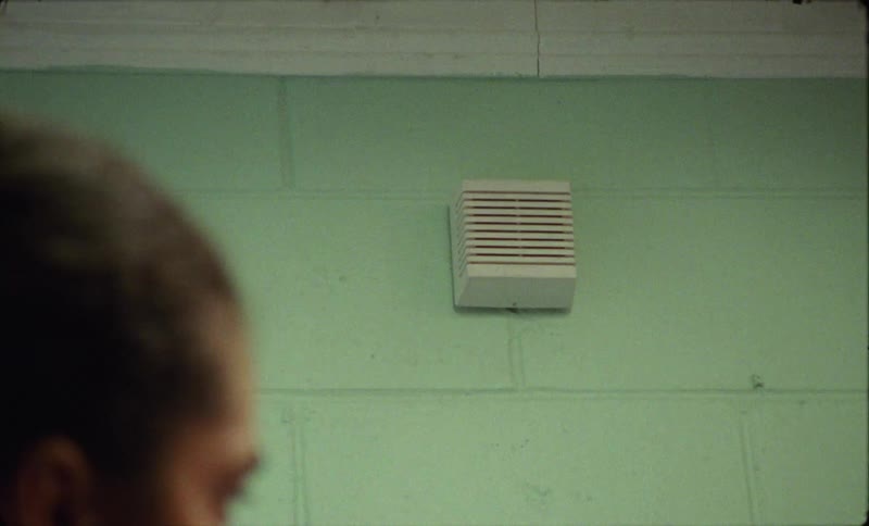 Person turns to look toward speaker mounted on green painted wall