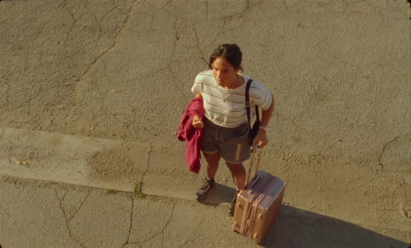 A young hispanic woman is standing outside with her luggage