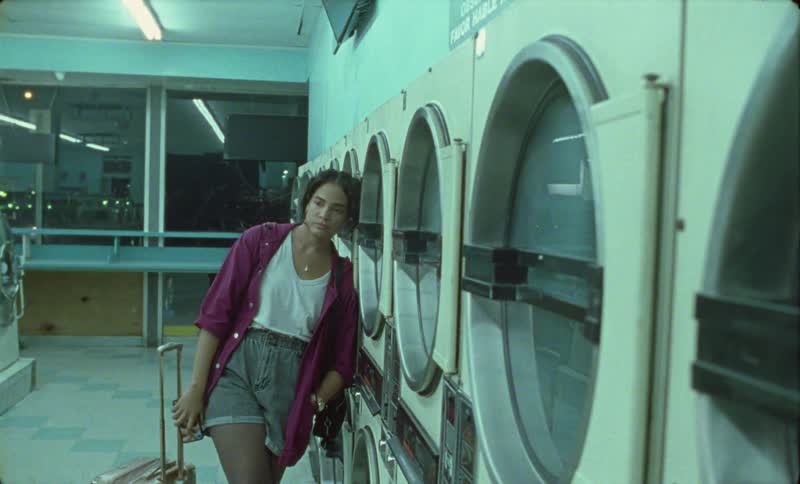 Woman tries to make call on smartphone while waiting for laundry at laundromat at night as traffic passes on nearby street