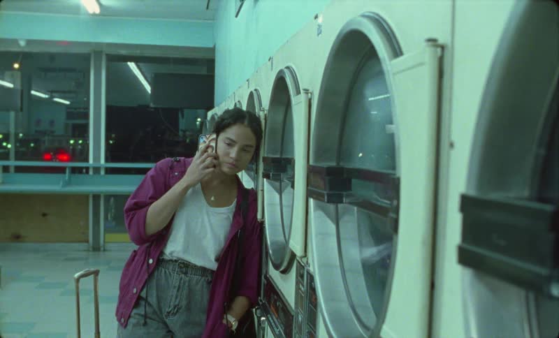 Young woman makes a call on her smartphone while waiting in the laundromat at night
