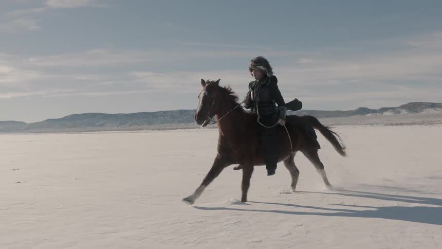 A man in a fur hat rides a horse through the snow