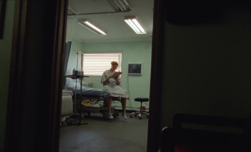 Young woman wearing a hospital gown fills a form sitting on a bed while the lights goes out