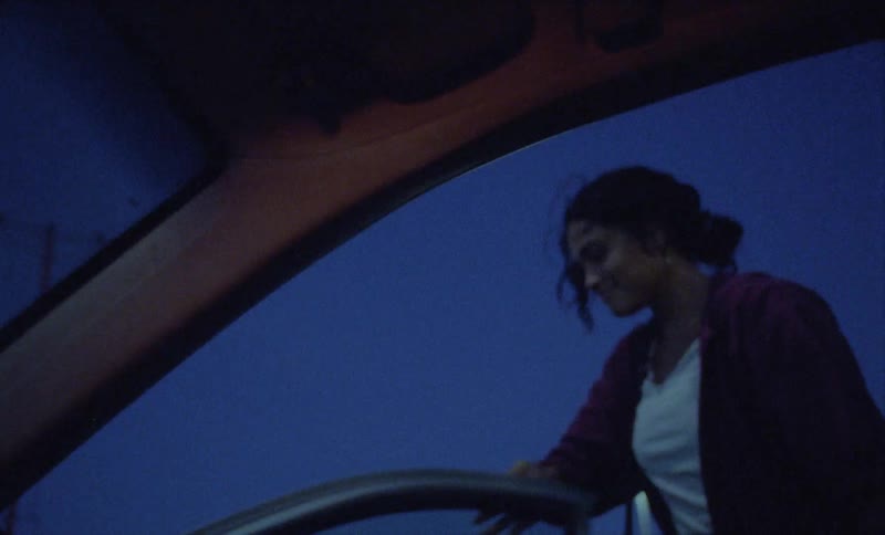 A woman is speaking to someone inside an automobile through the open door and she closes the door and walks away as an airplane flies overhead
