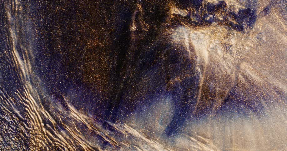 Waves and blobs of bright gold glittering ink moving and washing over dark blue ink