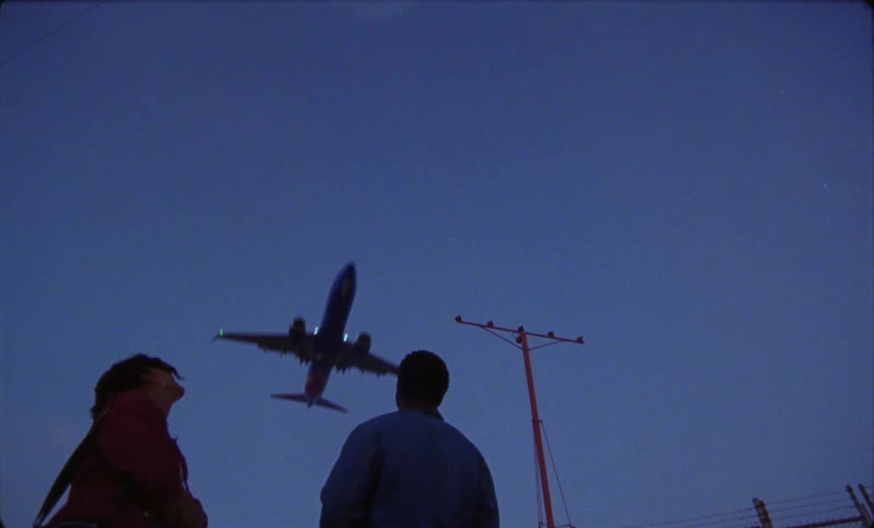 A man and woman stopping to watch an airplane fly overhead