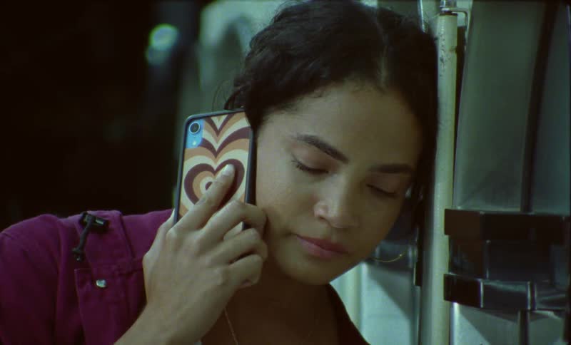 A woman talking on a phone leaning her head against washing machines in a laundromat