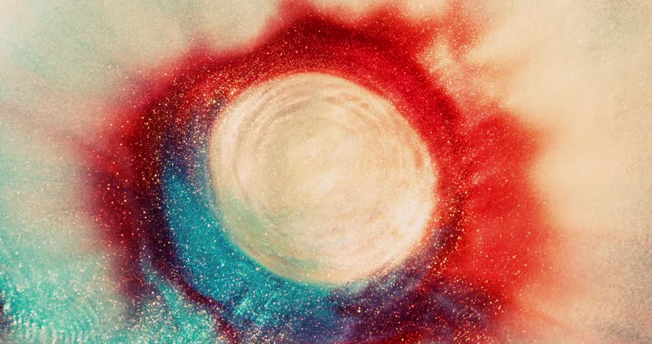 A red organic substance is moving in the darkness when it suddenly explodes and bright colors emerge from the ripples
