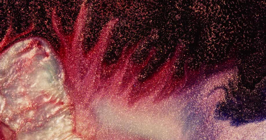 A red and pink sparkling liquid substance is moving as eruptions of a light color emerge from underneath