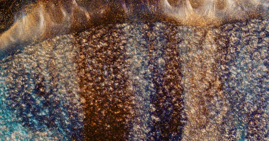 Waves of bright gold glittering ink washing away from bubbling dark blue ink