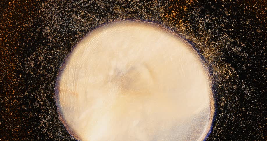 A blue and orange glittery environment moves and explodes from the center and growing into a white sphere surrounded by gold glitter before shrinking back down