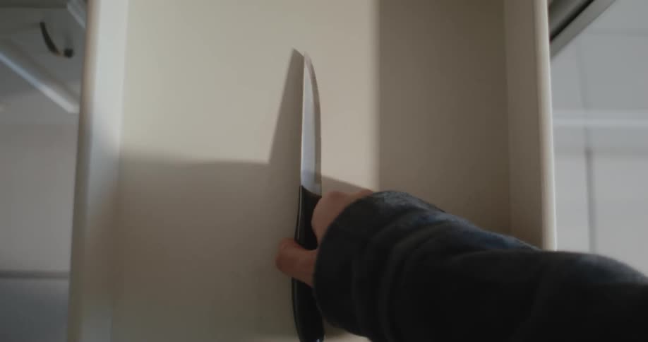 A hand opens a cabinet drawer displaying a single knife which is picked up and drawer closed