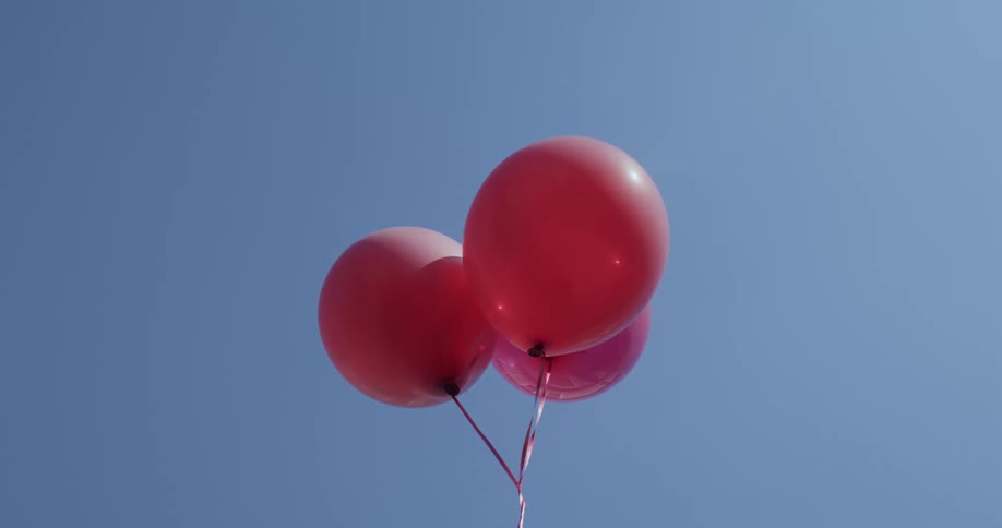 Three red balloons tied together floating on a clear blue sky at daytime
