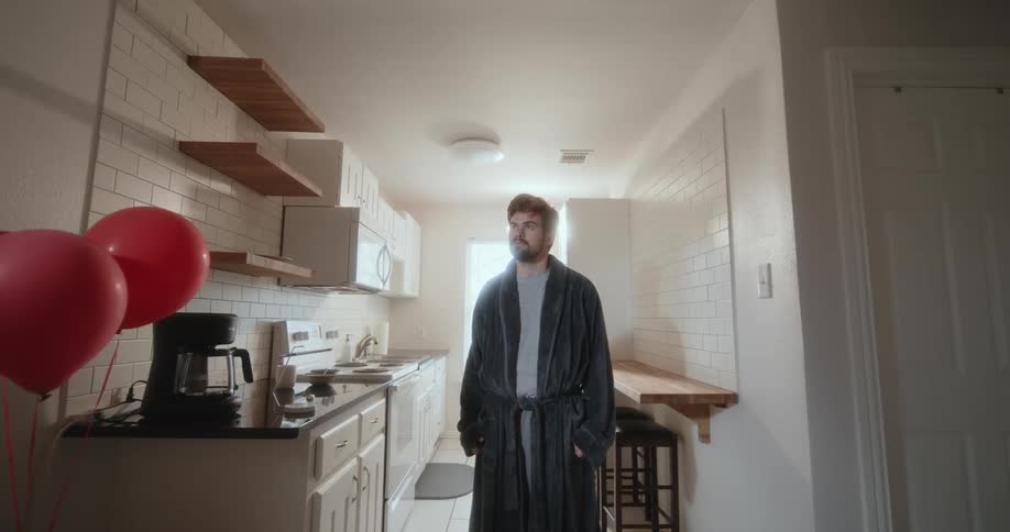 There is a young white man standing inside of his kitchen at his home
