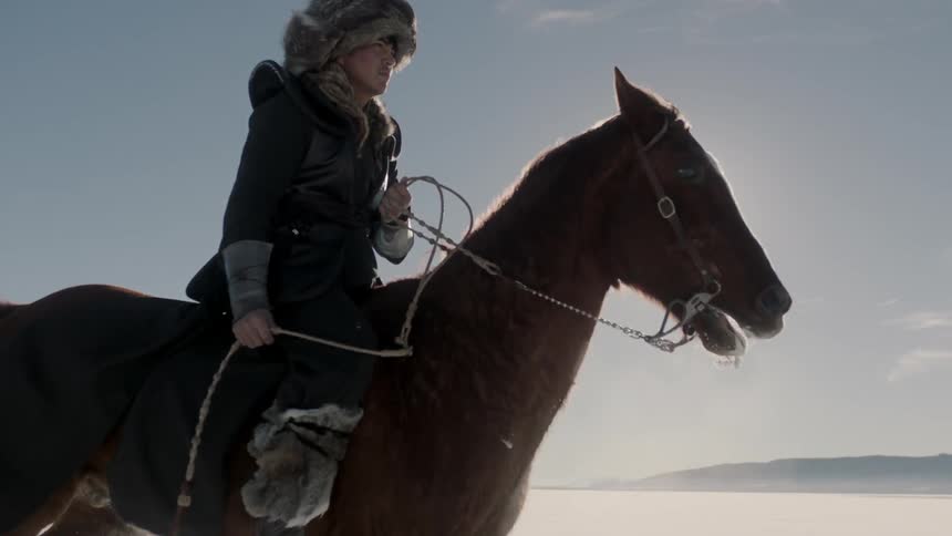 A man in a fur hat rides a horse through the snow