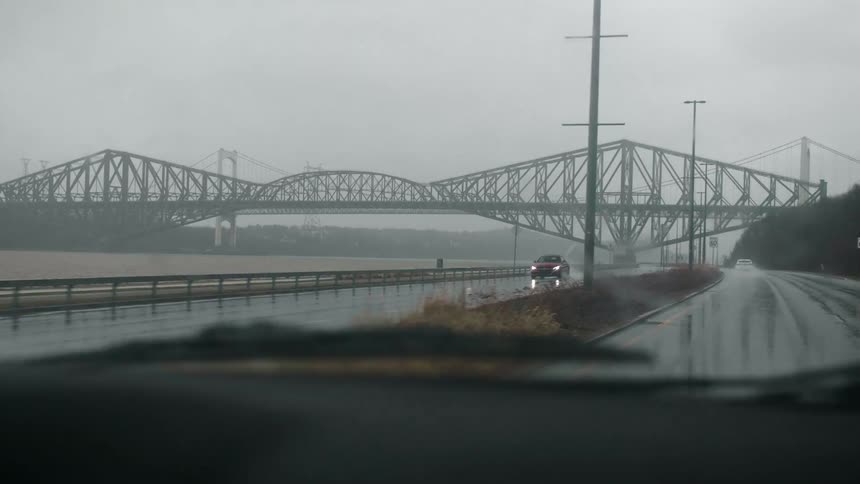 Windshield wipers work as car drives along wet roadway toward bridge