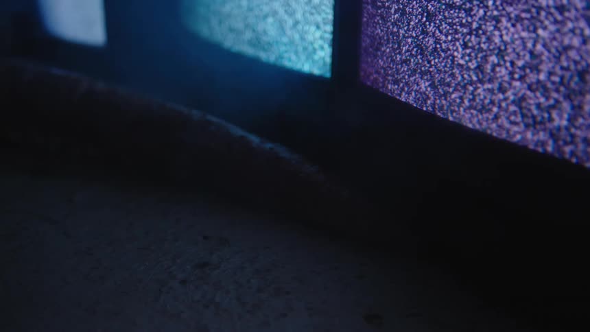 A row of television screens showing static on their screens lined up inside a dimly lit room