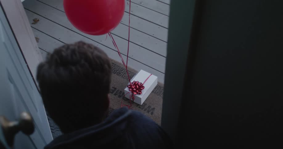 Man standing on the entrance door of his home looking at a present left on the porch