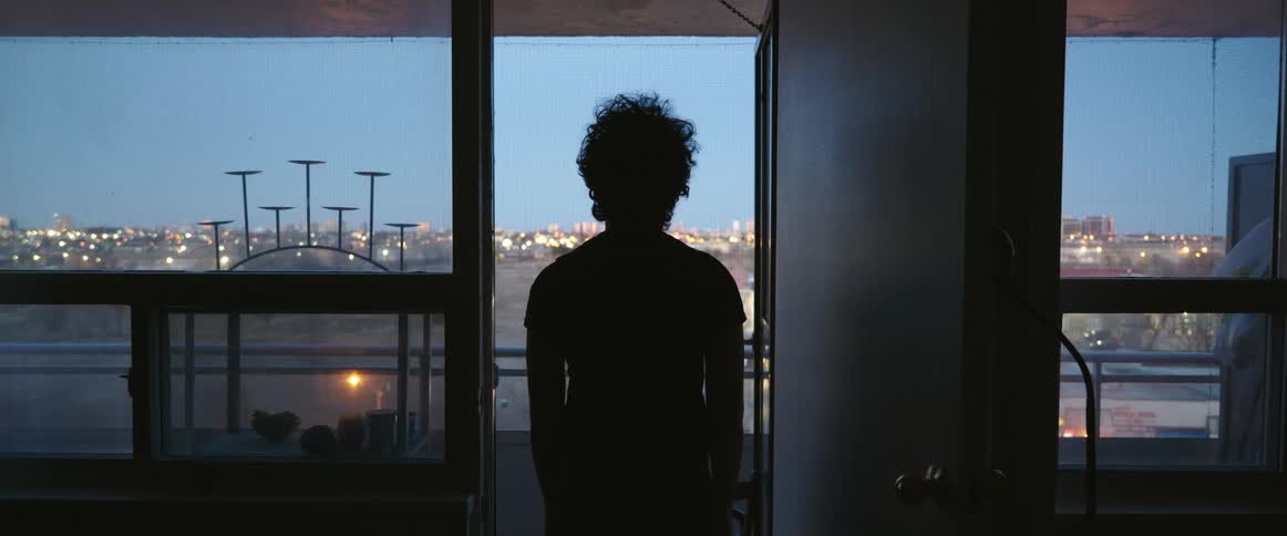 The silhouette of a person standing at the door to a balcony overlooking city lights