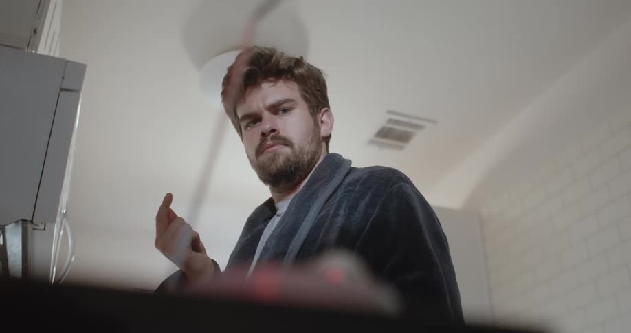 A man in a bathrobe looking confused while standing in his kitchen