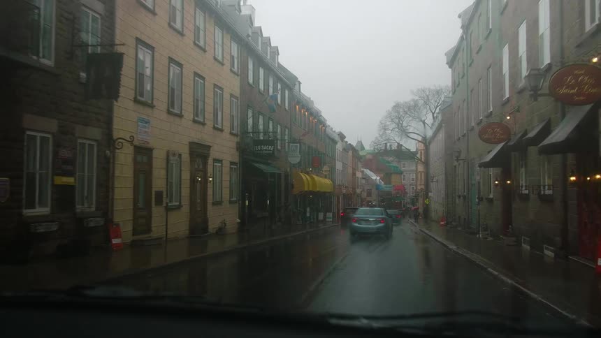 Cars driving on the narrow wet city streets while raining at daytime