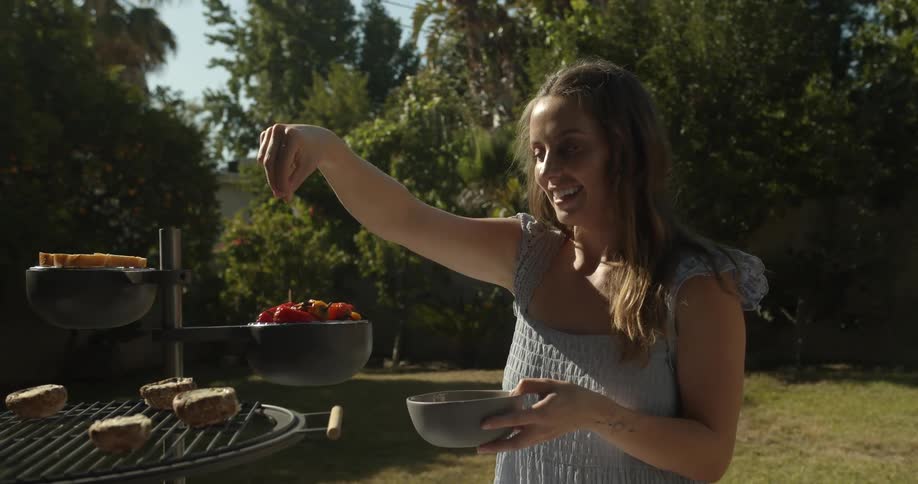 Woman smiles while seasoning food in elaborate barbecuing stand