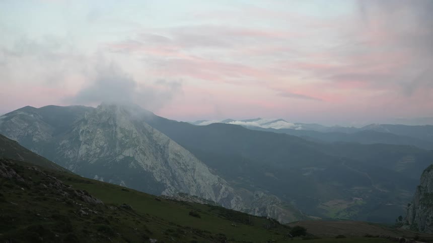A pink dawn rises over mountain ridges and peaks in Cantabria with clouds floating above