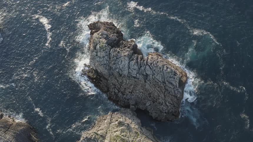 Aerial view of ocean waves breaking against big rock and cliff in the Spanish Atlantic