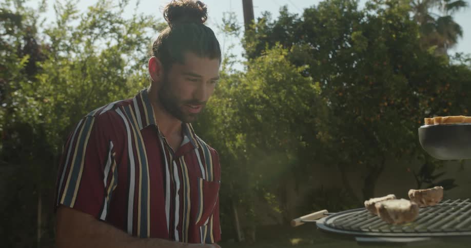 Young man serving pastries on a metal rack suspended over a table in the backyard at morning
