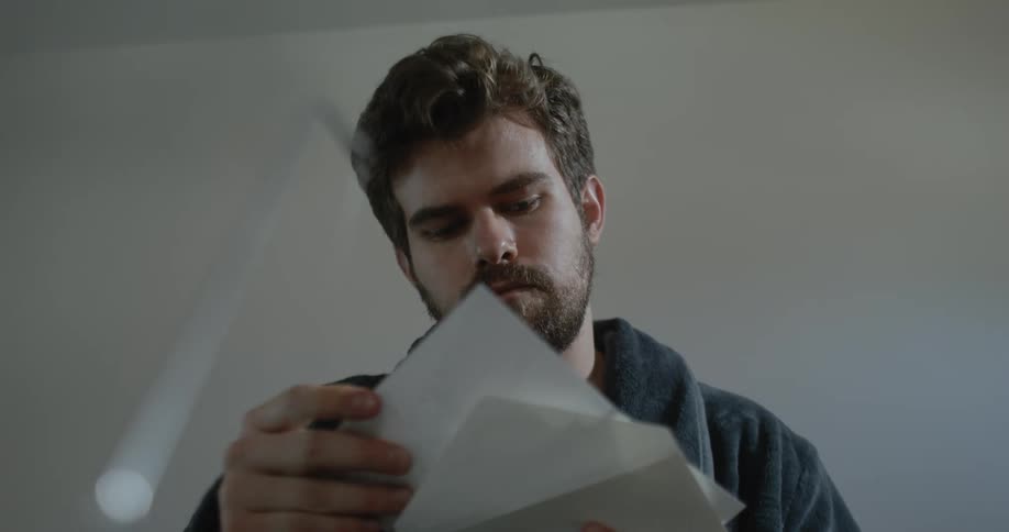 Man with beard and gray bathrobe opens envelope smiling slightly