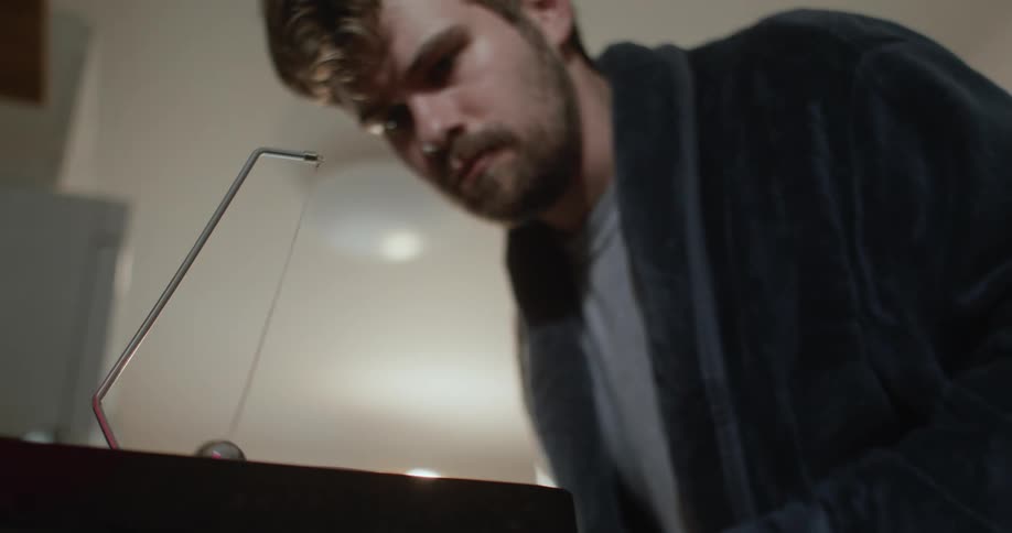 A man leaning over the counter reading a pamphlet starts a metal ball moving and vibrating