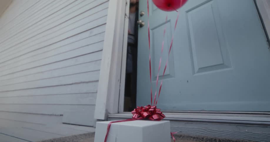 A white man opens the door and grabs the present from outside