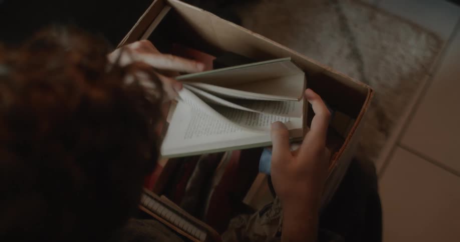 There is a man that is going through a box of books inside his room