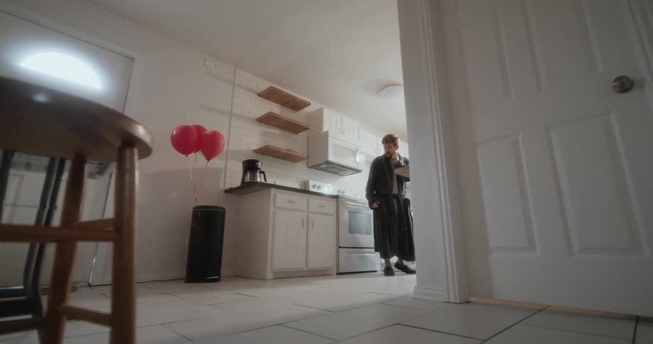 A young white man is standing inside of his kitchen at his home