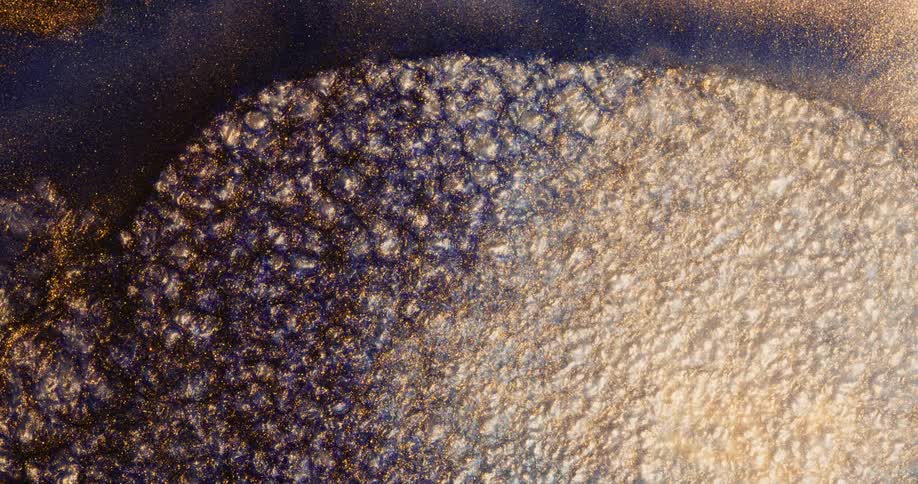 Orange glitter is shining in the darkness as an organic white layer of bubbles from underneath tears away the layer with the stars