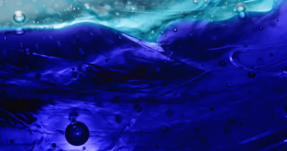 Round dark objects and bubble spheres are floating in a deep blue liquid substance and more larger bubbles are floating in a clear liquid with light blue wisps above