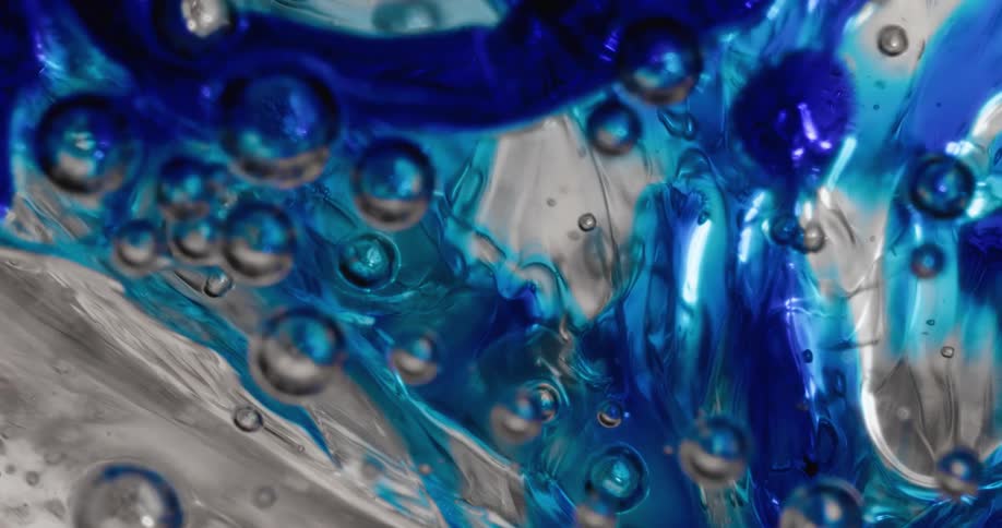 Bubble spheres reflect light and colors as they float in a moving mixture of light blue and electric blue substance on white