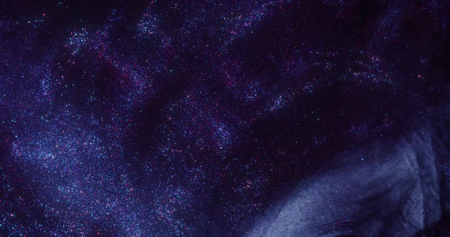 Blue and purple glitter expand against a black surface
