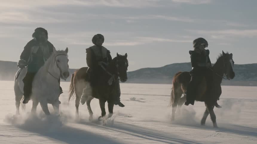 Three horses with riders run across a snow covered plain