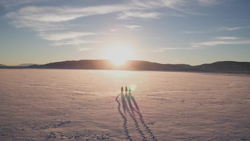 Three people walk across a flat land towards mountains