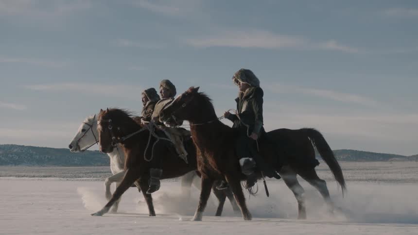 Three people ride horses across a snow covered field