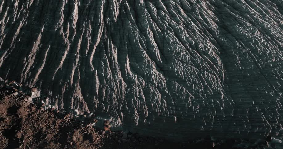 A mountain slope of lined rock and striations in sunshine and shadow