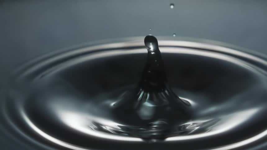Close up of drops of water falling on the calm surface creating ripples