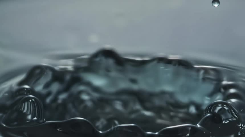 A drop of water hits the surface causing a circular splash and a peak