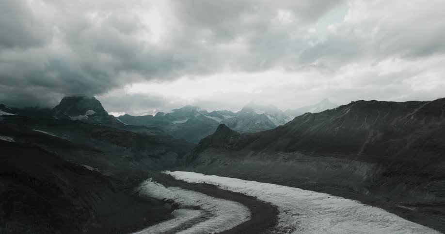 Heavy cloud cover over gray ridges and a snow covered trail