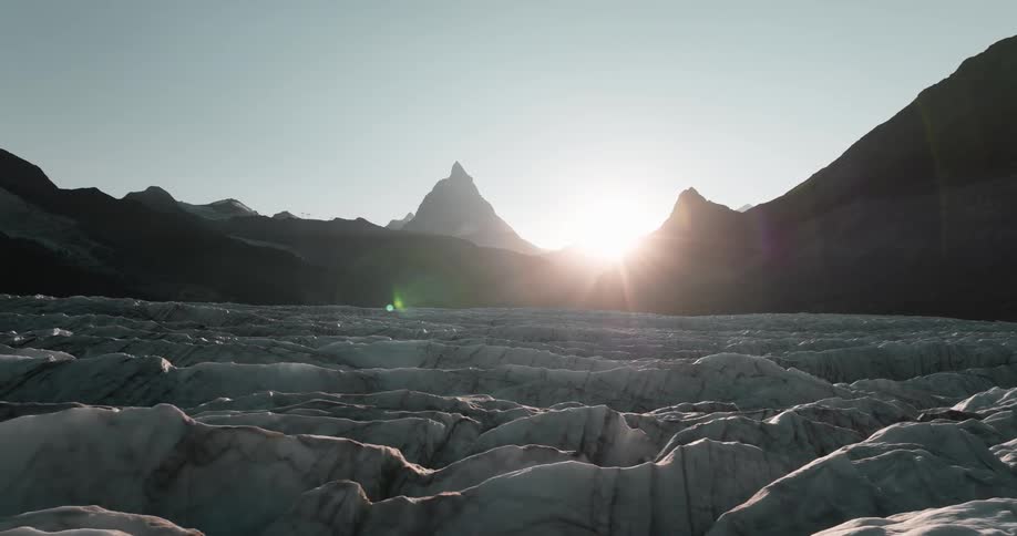 Bright sunlight shines between mountain peaks over an ice covered field