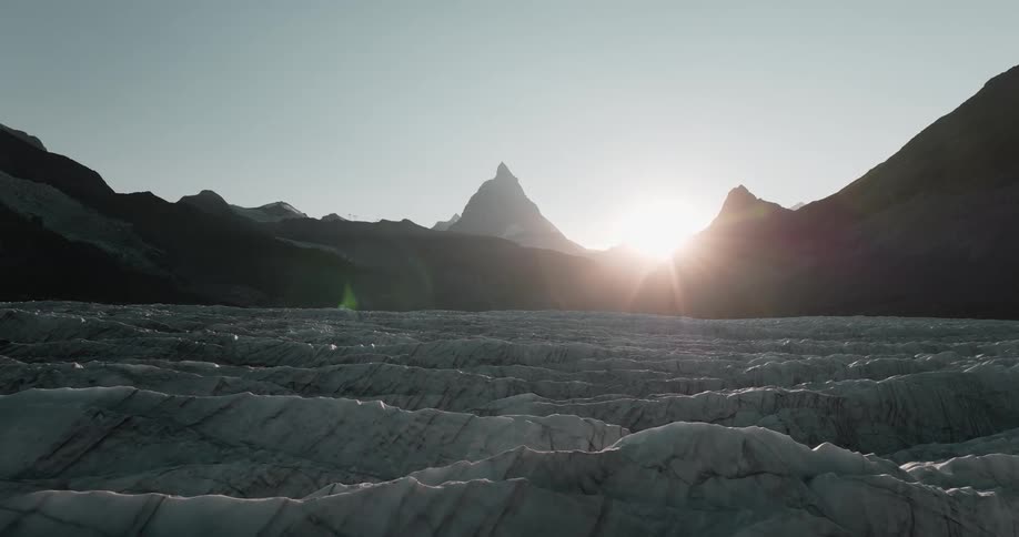 Gray and white ice ridges below the silhouette of mountain peaks and sunshine