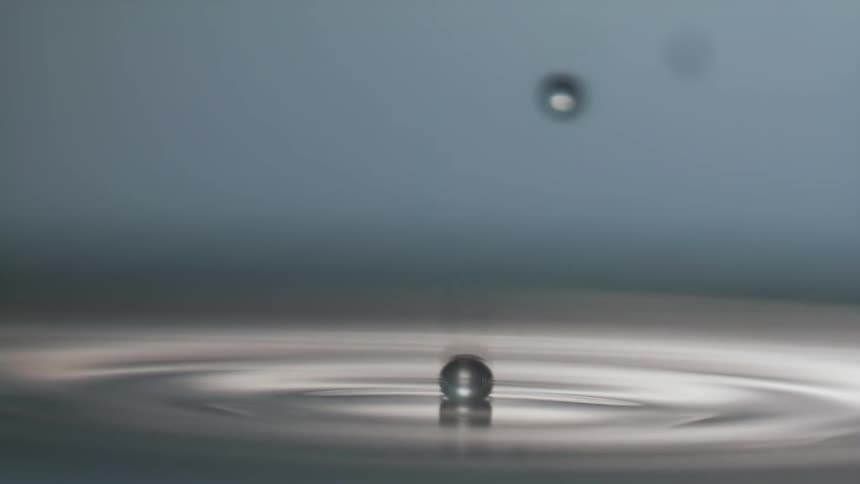 Round water droplets fall into the water and splash and ripple across the surface