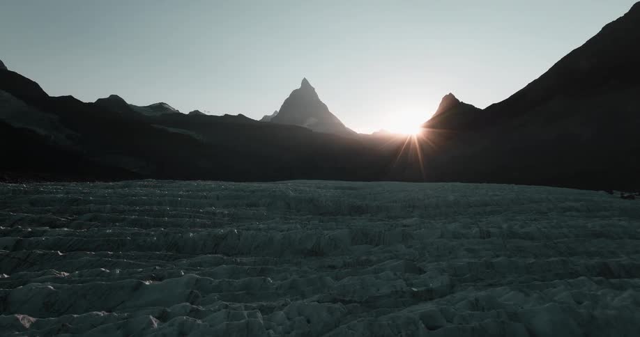 The sun shining over silhouetted mountains on a snowy morning