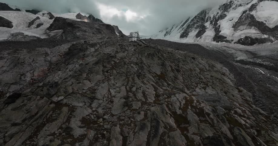 A barren rocky landscape with ice and snow and a single structure